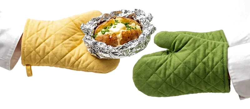 Two hands in oven mitts passing a baked potato in foil